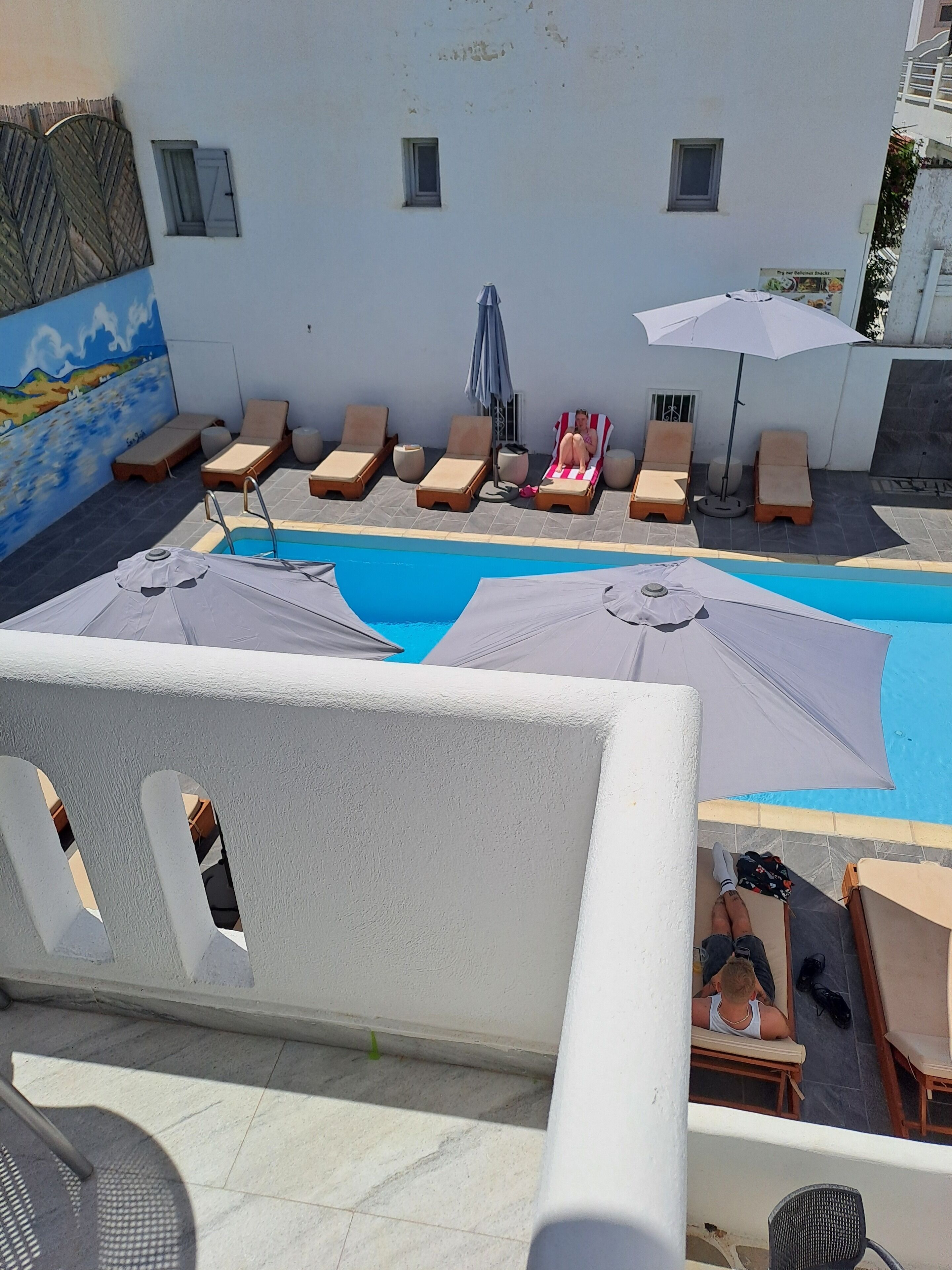Un espace piscine avec des chaises longues et des parasols, une fresque murale et un sol carrelé.