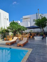 A poolside area with wooden loungers, a pool, and a person sitting at a table.