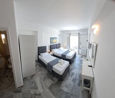A modern hotel room with two beds, a small desk, a mirror, and a bathroom visible through an open door.