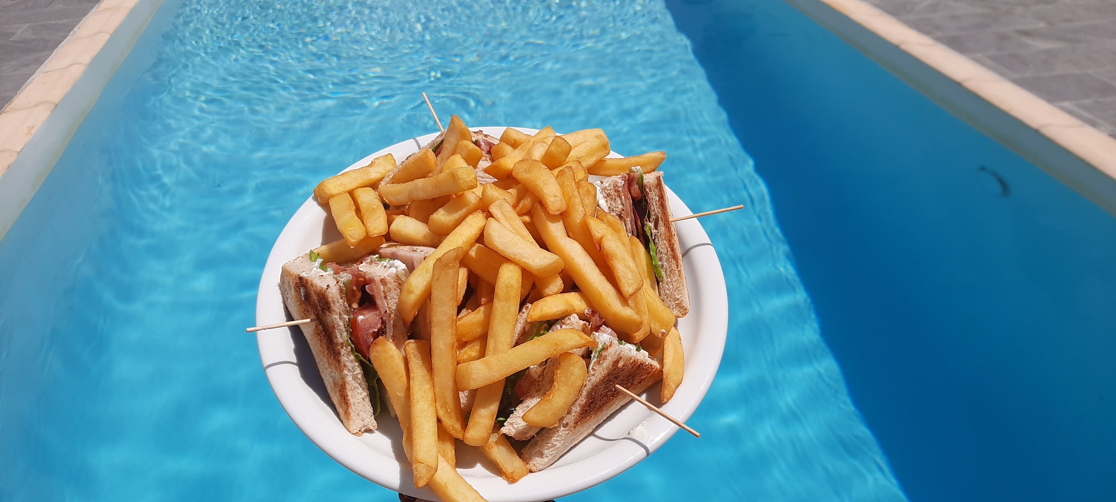 A plate of food with French fries and sandwiches by a pool.