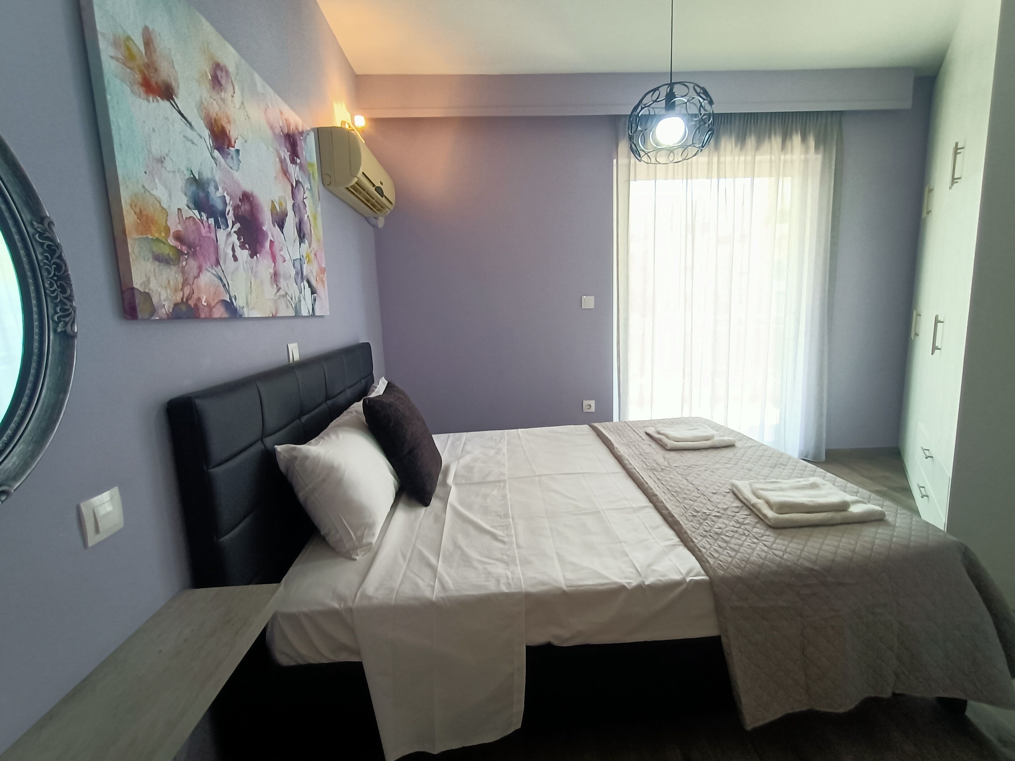 A bedroom with a bed, a wall-mounted air conditioner, a ceiling light fixture, and a window with curtains.
