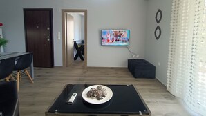 A modern living room with a dining area, a black table with a plate of snacks, a TV on the wall, and a patterned curtain. - Highlighted Retreat (Athens)