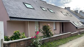 A residential building with a sloped roof, multiple windows, and a garden with flowers. - Appartement 2pers Le Pouldu, Proche Plages (Clohars-Carnoët)