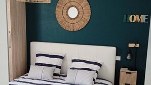 A bedroom with a bed, bedside table, lamp, and wall decor. - Appartement 2pers Le Pouldu, Proche Plages (Clohars-Carnoët)