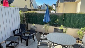 A patio area with a round table and four chairs, a small round table, and a red umbrella. - Appartement 2pers Le Pouldu, Proche Plages (Clohars-Carnoët)