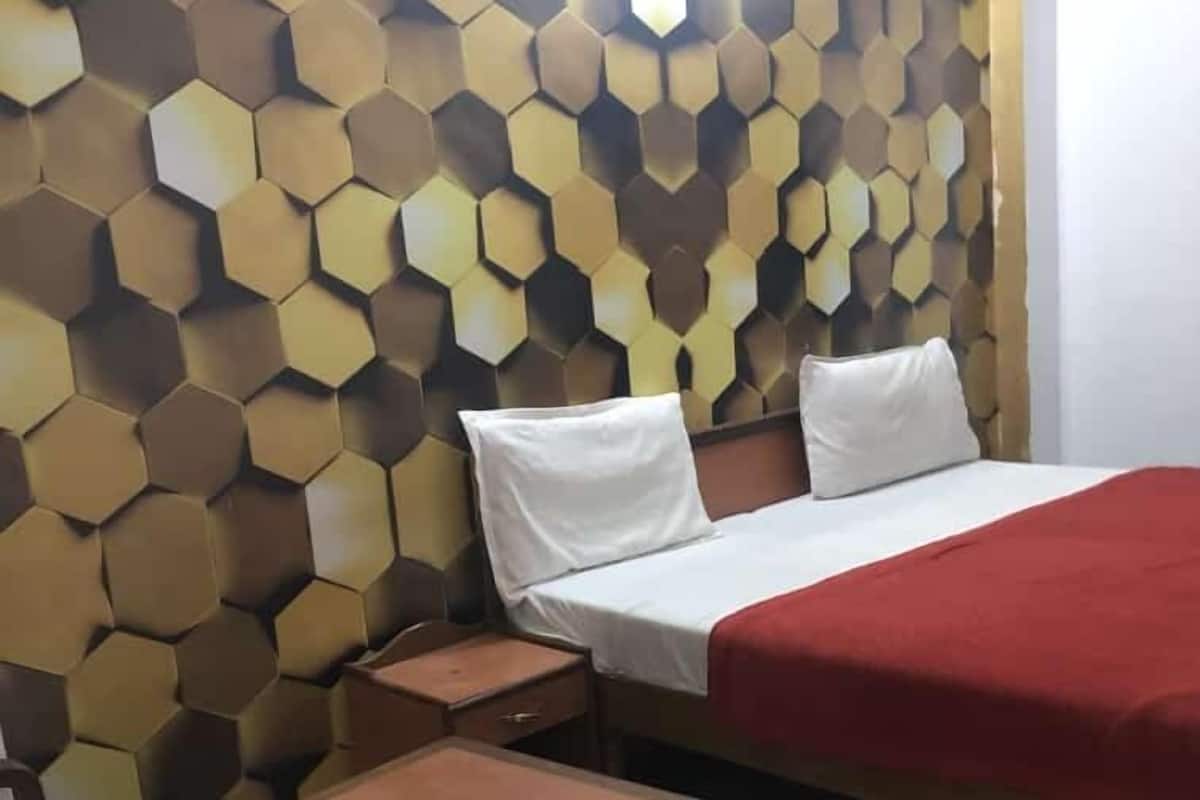 A hotel room with a hexagonal patterned wall, a bed with white and red bedding, a wooden nightstand, and a wooden chair.