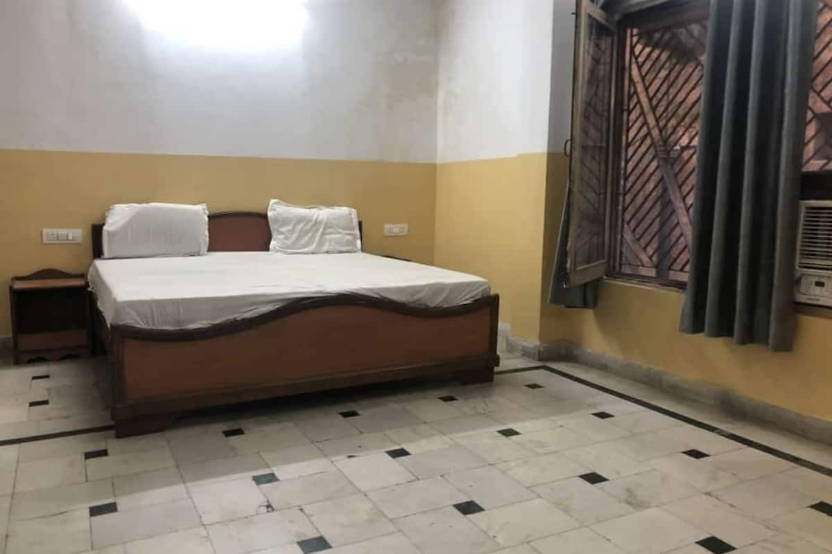 A bedroom with a bed, a nightstand, a window with a metal grille, and a wall-mounted air conditioning unit.