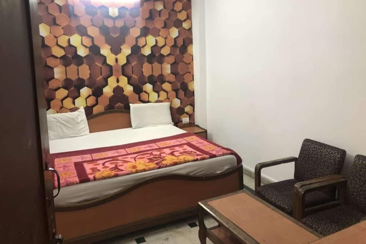 A single bed with a patterned headboard, a bedside table, and a chair in a room with white walls.