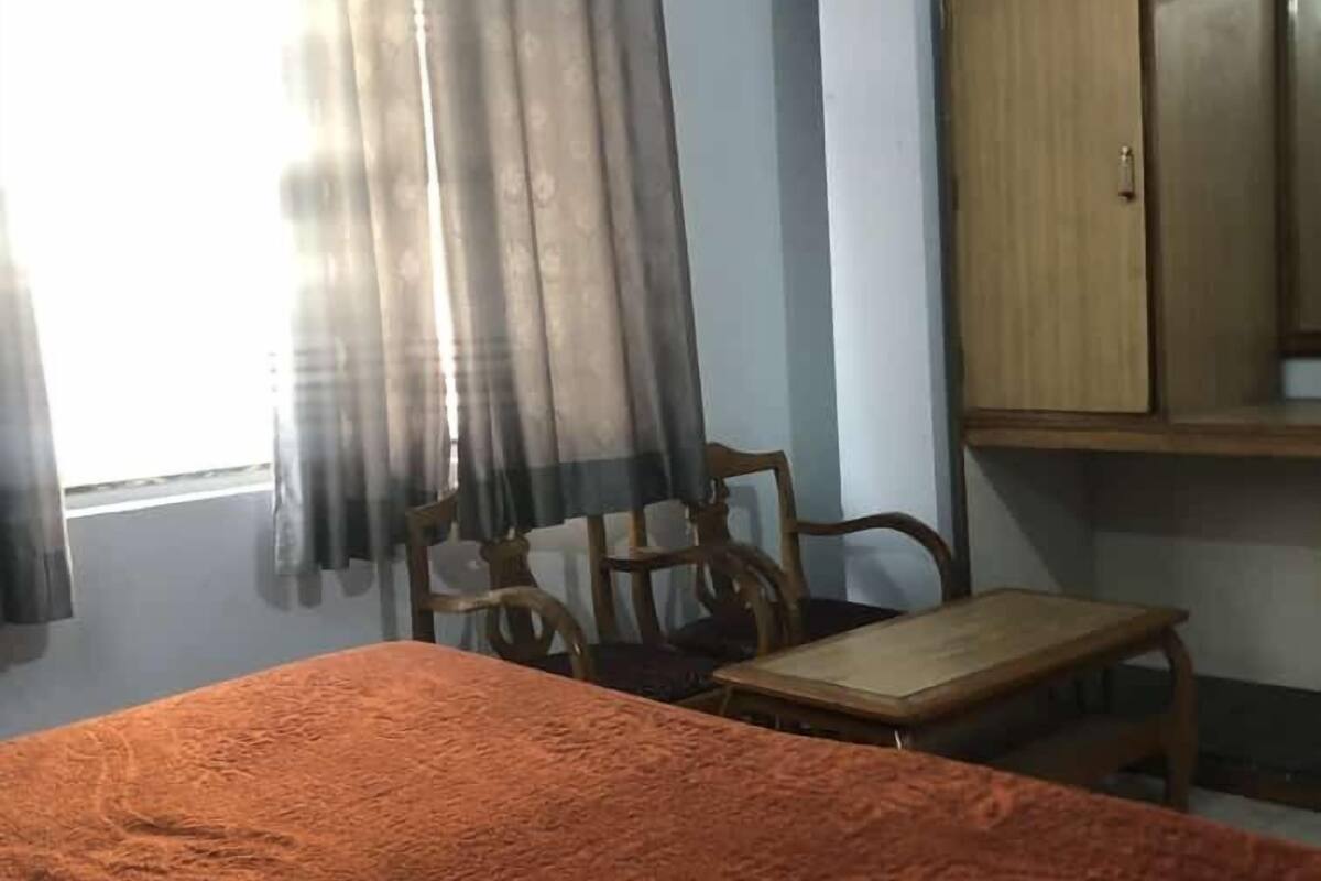 A room with a bed, a wooden cabinet, a chair, and a window with curtains.