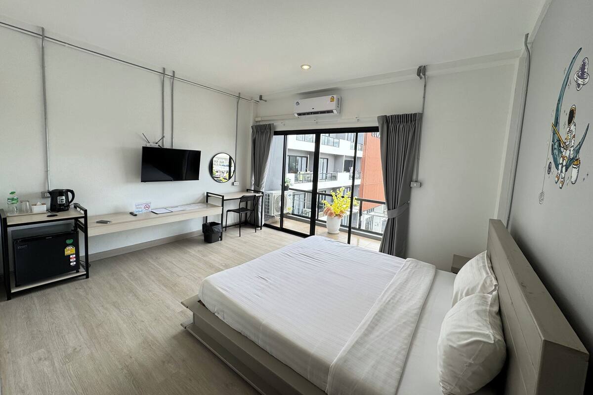 A hotel room with a bed, a desk, a TV, and a balcony with a view.
