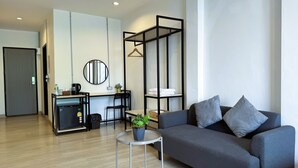 A modern living room with a grey sofa, a small round table with a plant, a coffee machine, and a black metal shelf unit. - Luka House (Lam Luk Ka)