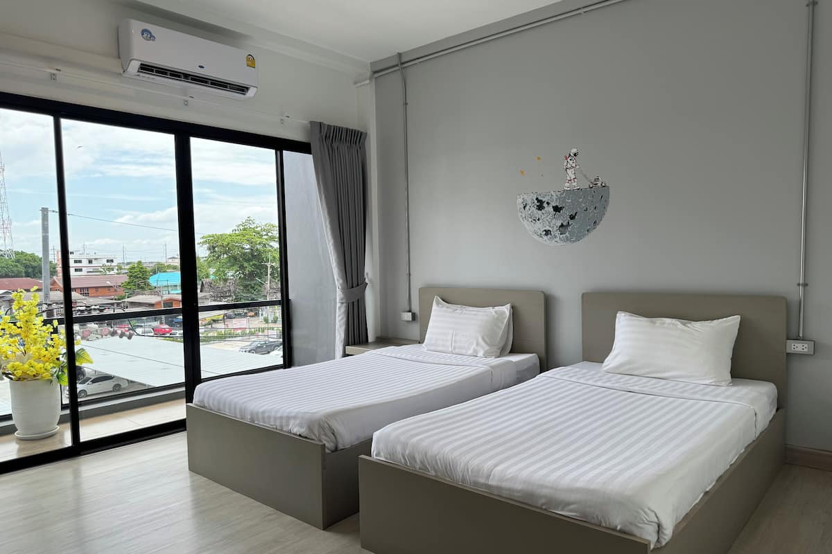 A hotel room with two beds, a large window with a view of the city, an air conditioning unit, and a wall-mounted decorative item.