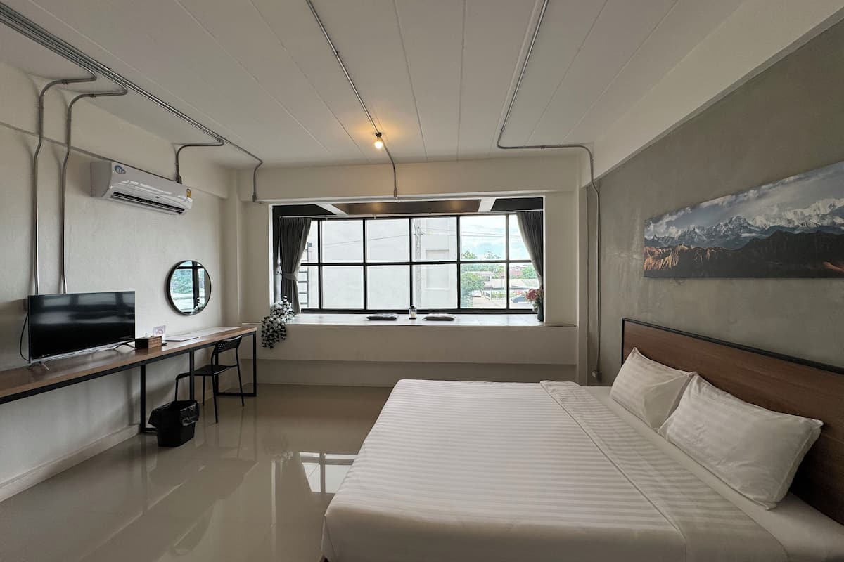 A hotel room with a bed, a desk, a chair, a TV, and a window with a view of mountains.
