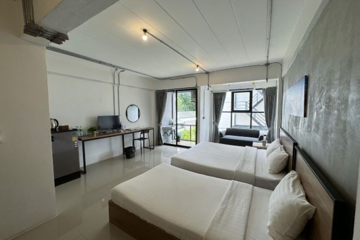 A hotel room with two beds, a desk with a computer, and a view of the outdoors.