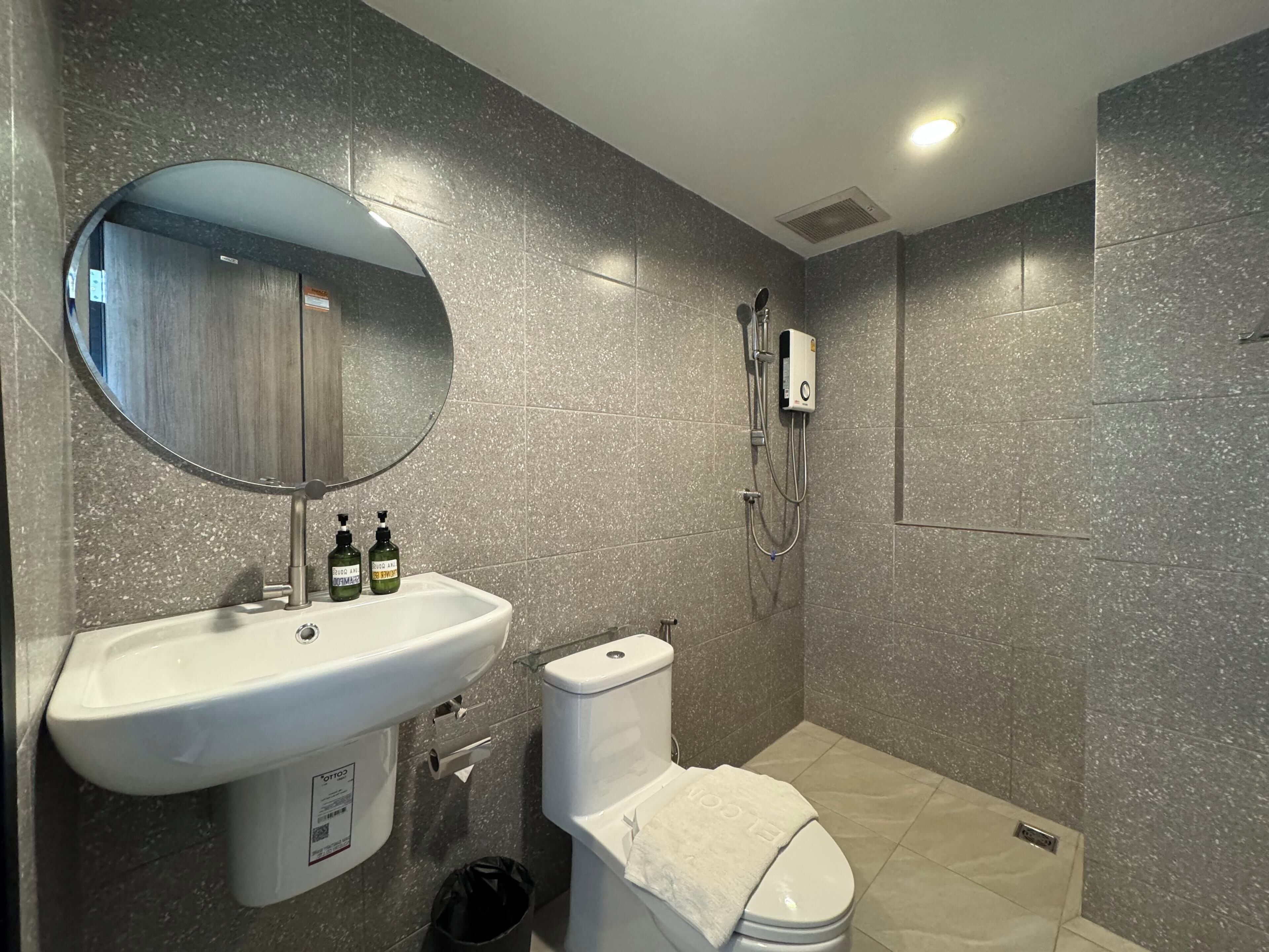Un baño con lavamanos blanco, espejo, inodoro, zona de ducha y un cubo de basura.
