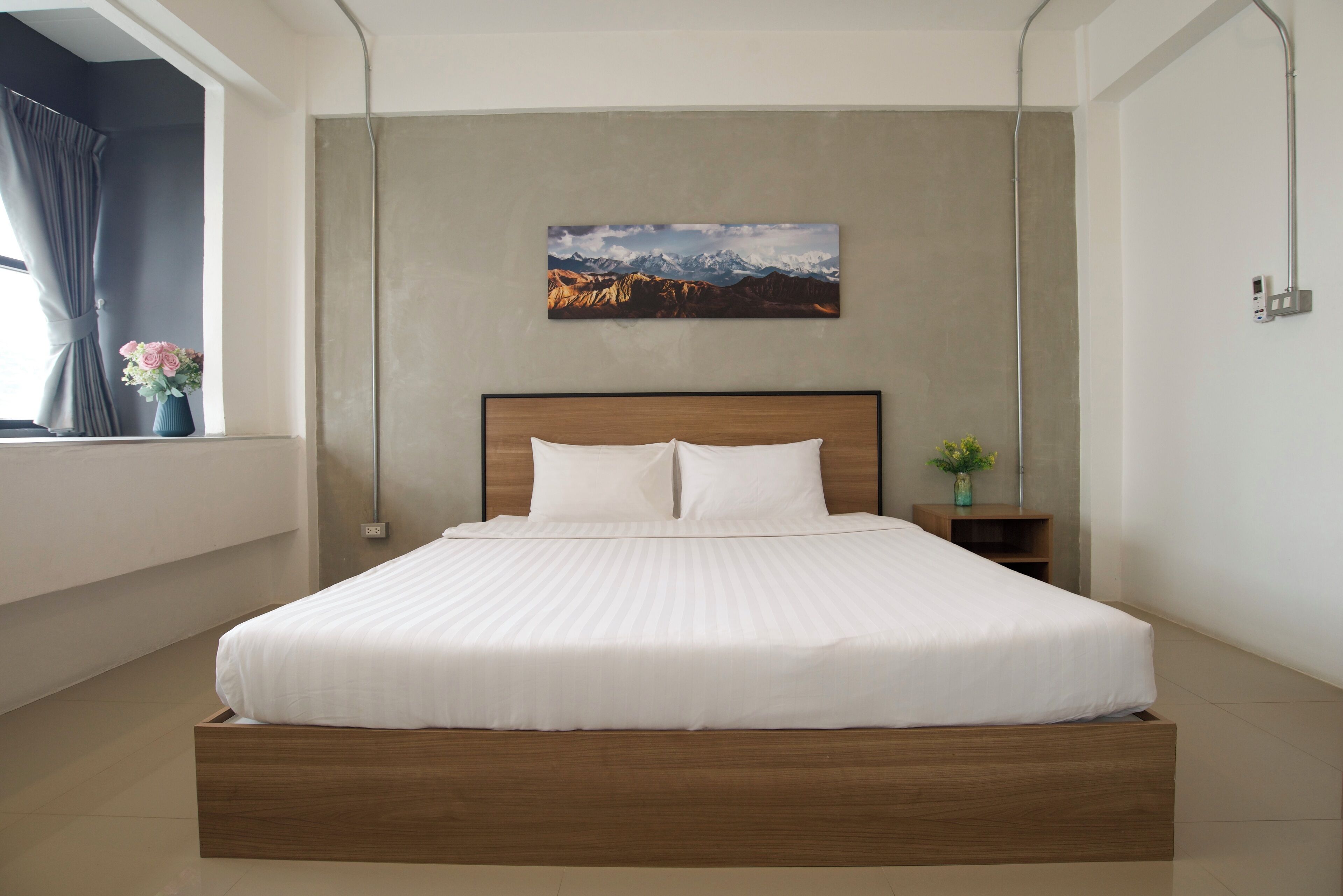 A modern bedroom with a large bed, a nightstand, a wall-mounted lamp, and a window with curtains.
