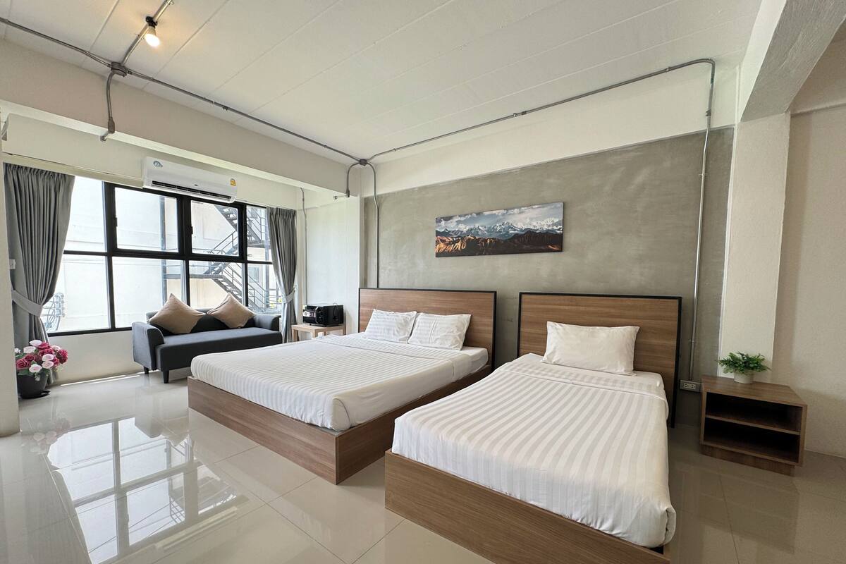 A modern hotel room with two beds, a sofa, a small table, and a large window with curtains.