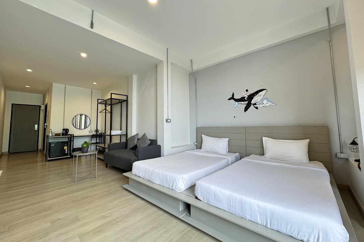 A modern hotel room with two beds, a seating area with a sofa, a small table, and a mirror.