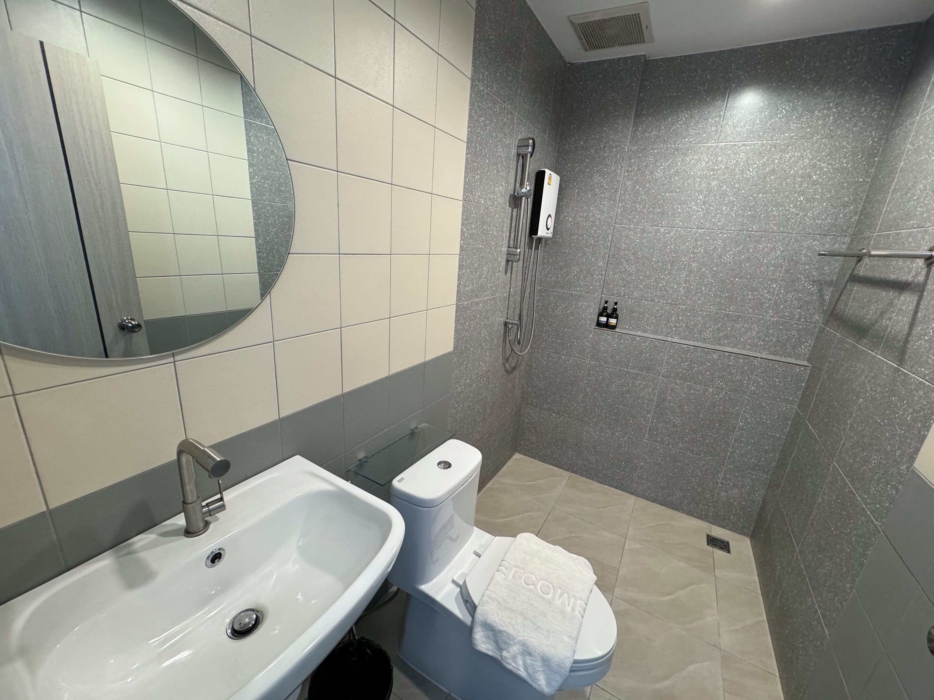 Un baño moderno con lavamanos, inodoro y ducha blancos. Una toalla está colgada sobre el inodoro.
