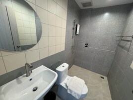 Un baño moderno con lavamanos, inodoro y ducha blancos. Una toalla está colgada sobre el inodoro.