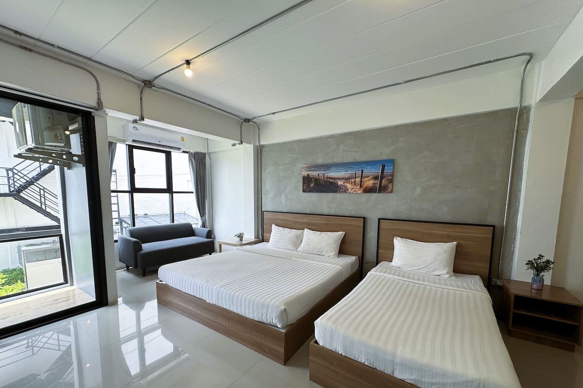 A modern hotel room with two beds, a sofa, a painting, and a view of the outdoors.