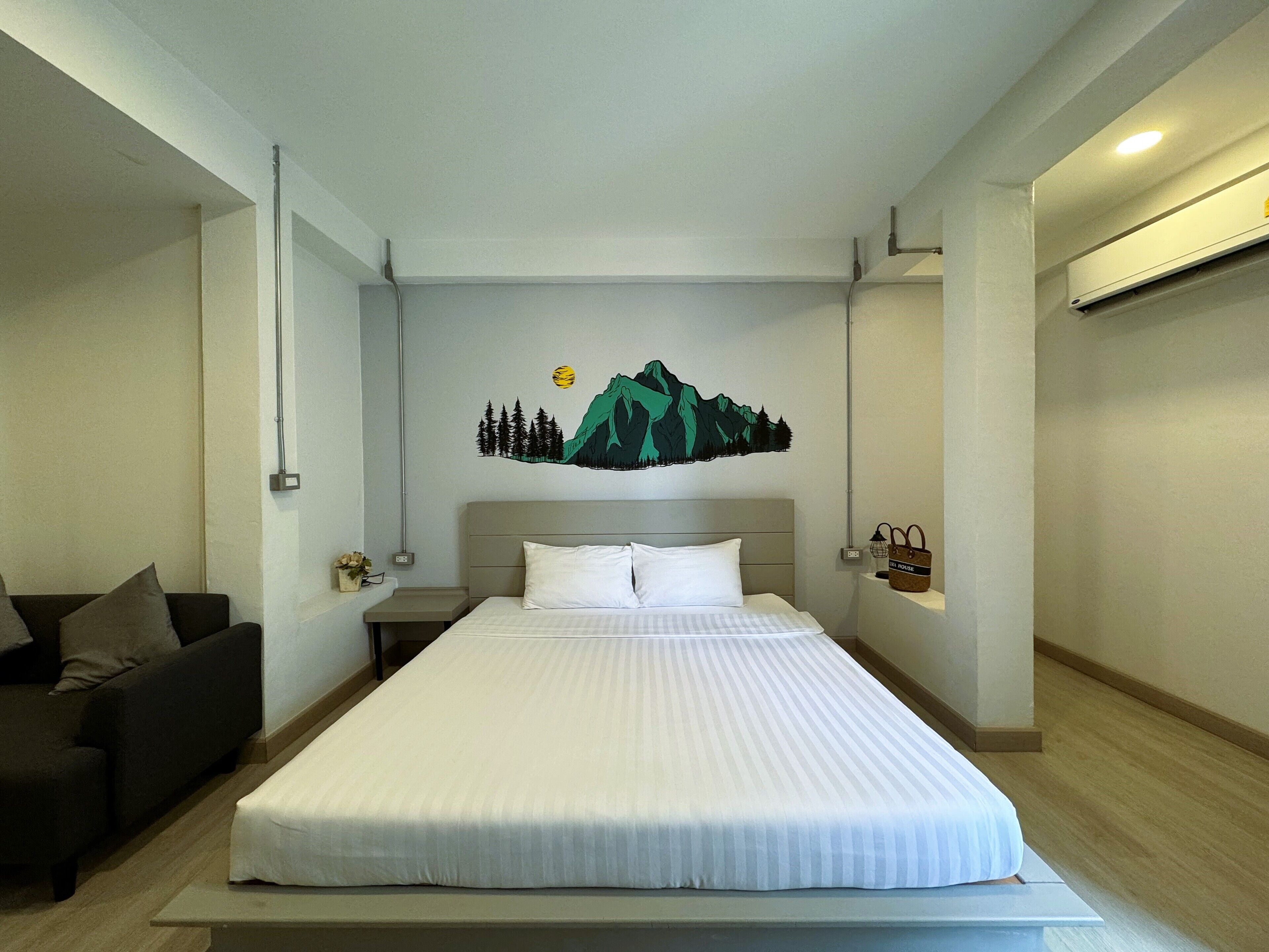 A hotel room with a bed, a nightstand, a lamp, a wall-mounted shelf, and a couch.