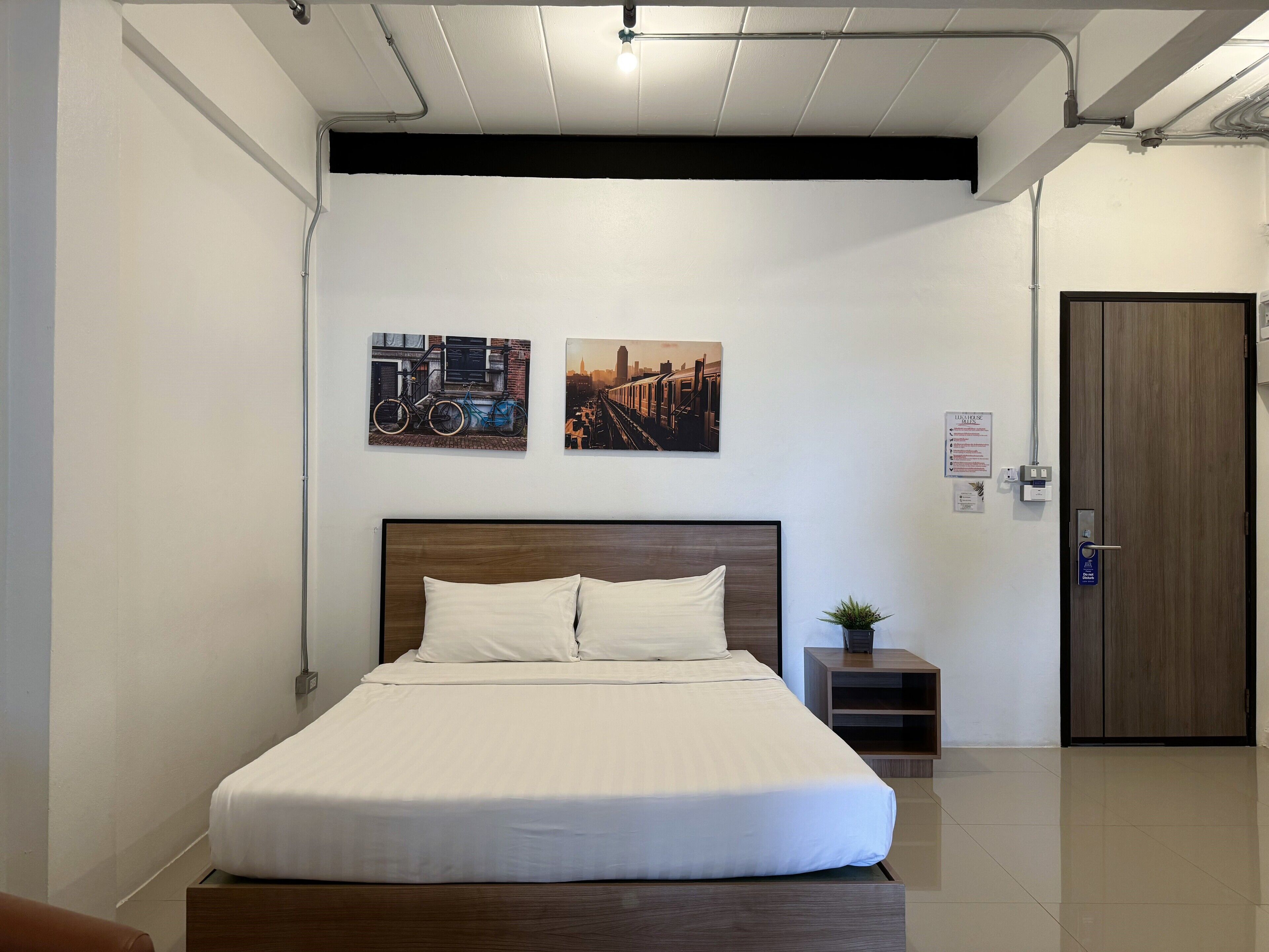 A neatly made bed with white linens, a wooden headboard, and two wall-mounted pictures of bicycles.