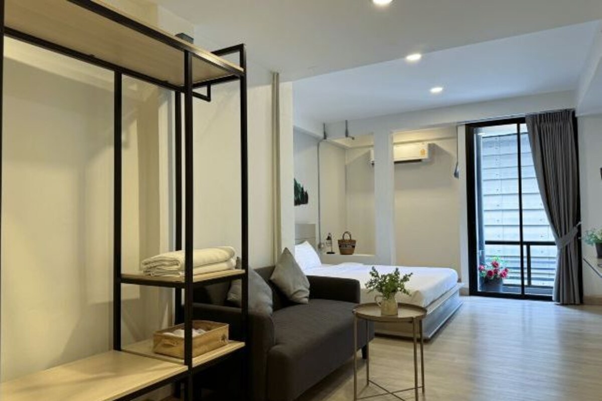 A modern hotel room with a bed, a sofa, a small table, and a large window with curtains.