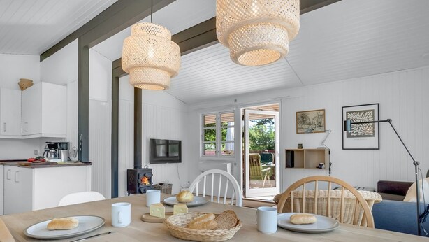 A modern kitchen with white cabinetry, a wood-burning stove, and a dining area with a wooden table set for breakfast. - "Borghild" - 500m from the sea by Interhome (Gedser)