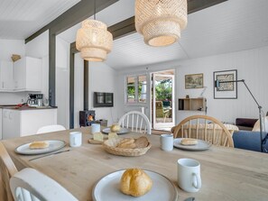 Une cuisine moderne avec des meubles blancs, un poêle à bois et un coin repas doté d’une table en bois, mise pour le petit-déjeuner.