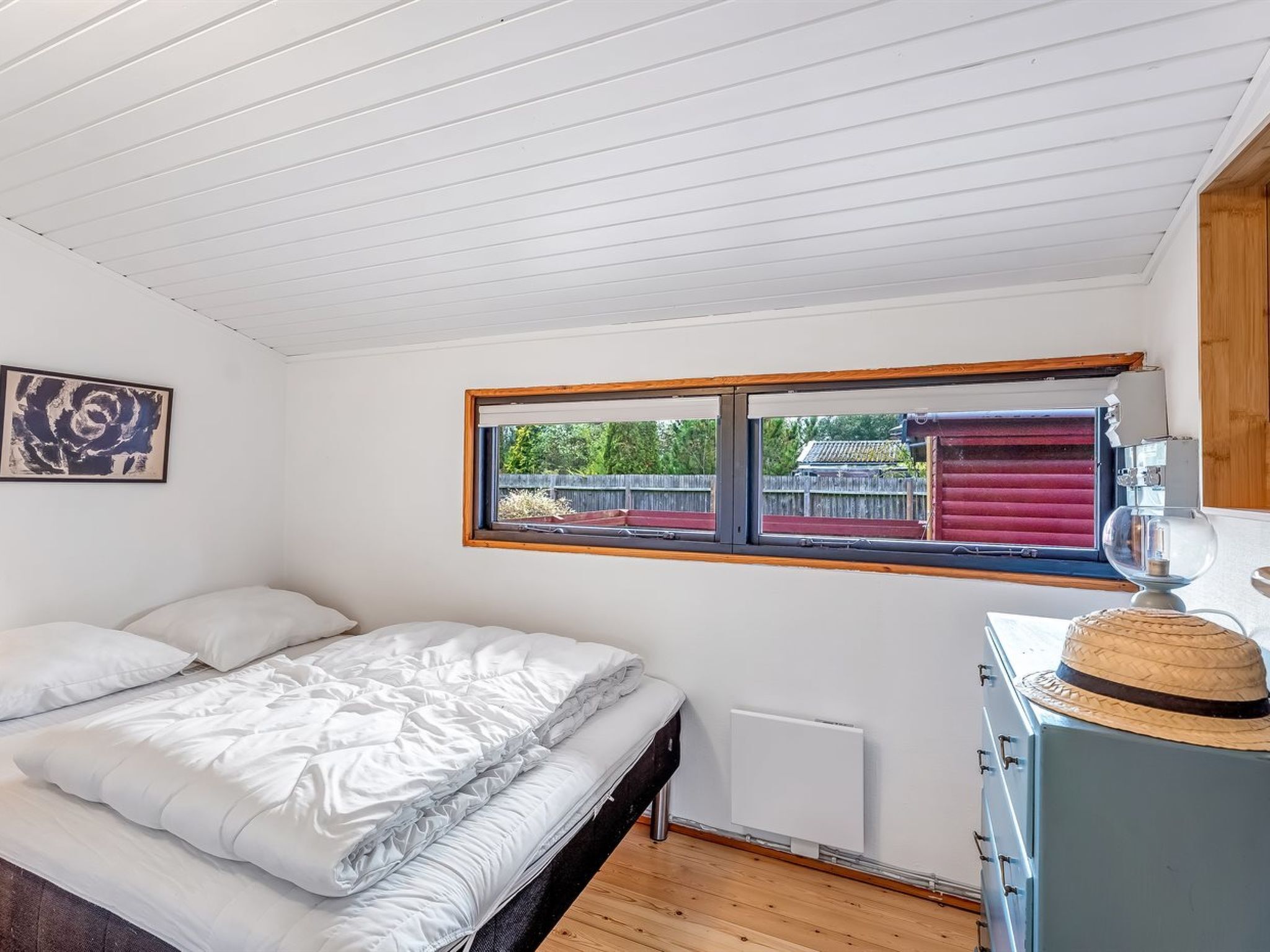 Een slaapkamer met een bed, een raam, een radiator en een houten dressoir.
