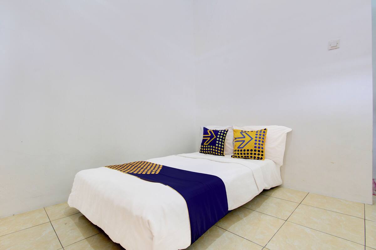 Ein Einzelbett mit weißblauer Bettdecke, zwei gemusterte Kissen und eine schlichte weiße Wand.