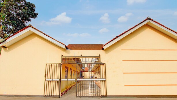 A building with a yellow facade, a metal gate, and a staircase leading to a higher level. - Hotel O Guest House Wijaya Syariah Near alun alun kota purwokerto (Purwokerto)