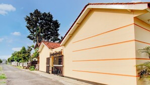 A residential street with a beige house featuring orange horizontal lines, a gated entrance, and a tiled roof. - Hotel O Guest House Wijaya Syariah Near alun alun kota purwokerto (Purwokerto)