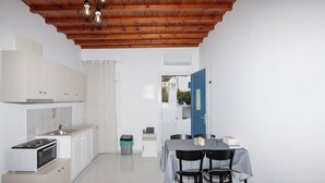 Une pièce compacte comprenant un coin cuisine, un espace repas avec deux chaises, un lit et un plafond en bois.