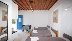 Une chambre d’hôtel avec deux lits, un bureau et une chaise. Il y a une porte bleue et une fenêtre.