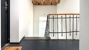 A staircase with a brick ceiling, a black railing, and a white wall.