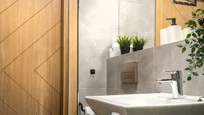 A modern bathroom with a wooden door, a white sink, and a toilet.
