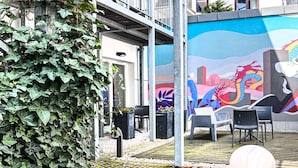 A courtyard with a concrete planter with flowers, a tiled floor, and a mural on the wall. - Cozy Apartment with A/C for couples, City Center 2, Różana (Kraków)