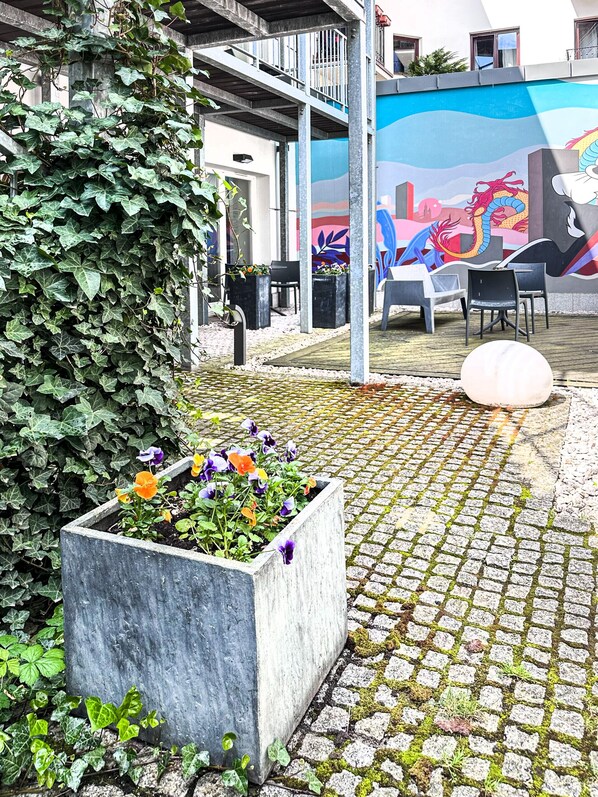 Un cortile con un vaso in cemento pieno di fiori, un pavimento piastrellato e un murale sulla parete.