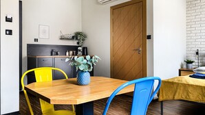Eine kleine Küche mit einem Holztisch, gelben und blauen Stühlen, einem Blumentopf und einer Holztür.