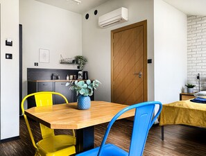 A compact kitchen with a wooden table, yellow and blue chairs, a potted plant, and a wooden door. - Cozy Apartment with A/C for couples, City Center 2, Różana (Kraków)