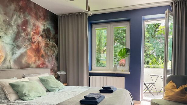 Une chambre avec un lit, une fenêtre donnant sur un paysage verdoyant, une plante sur le rebord de la fenêtre et une chaise.