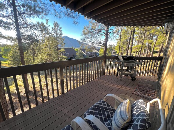 Une terrasse en bois offrant une vue sur une montagne et des arbres. On y trouve un barbecue et du mobilier d’extérieur.