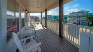 Een overdekt terras met witte stoelen en uitzicht op omliggende huizen.