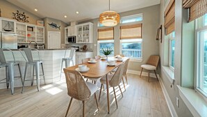 Een moderne keuken met witte kasten, een houten eettafel en rieten stoelen.