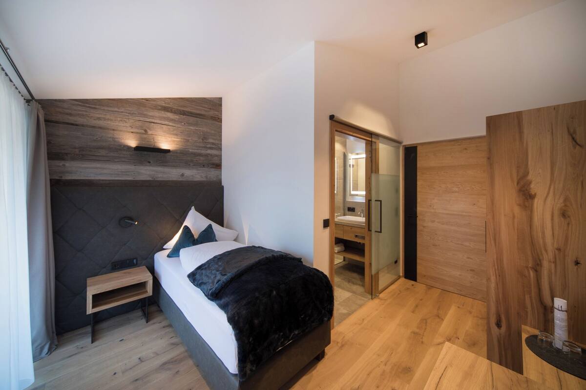 A modern bedroom with a large bed, a nightstand, a wooden headboard, and a wooden wardrobe.
