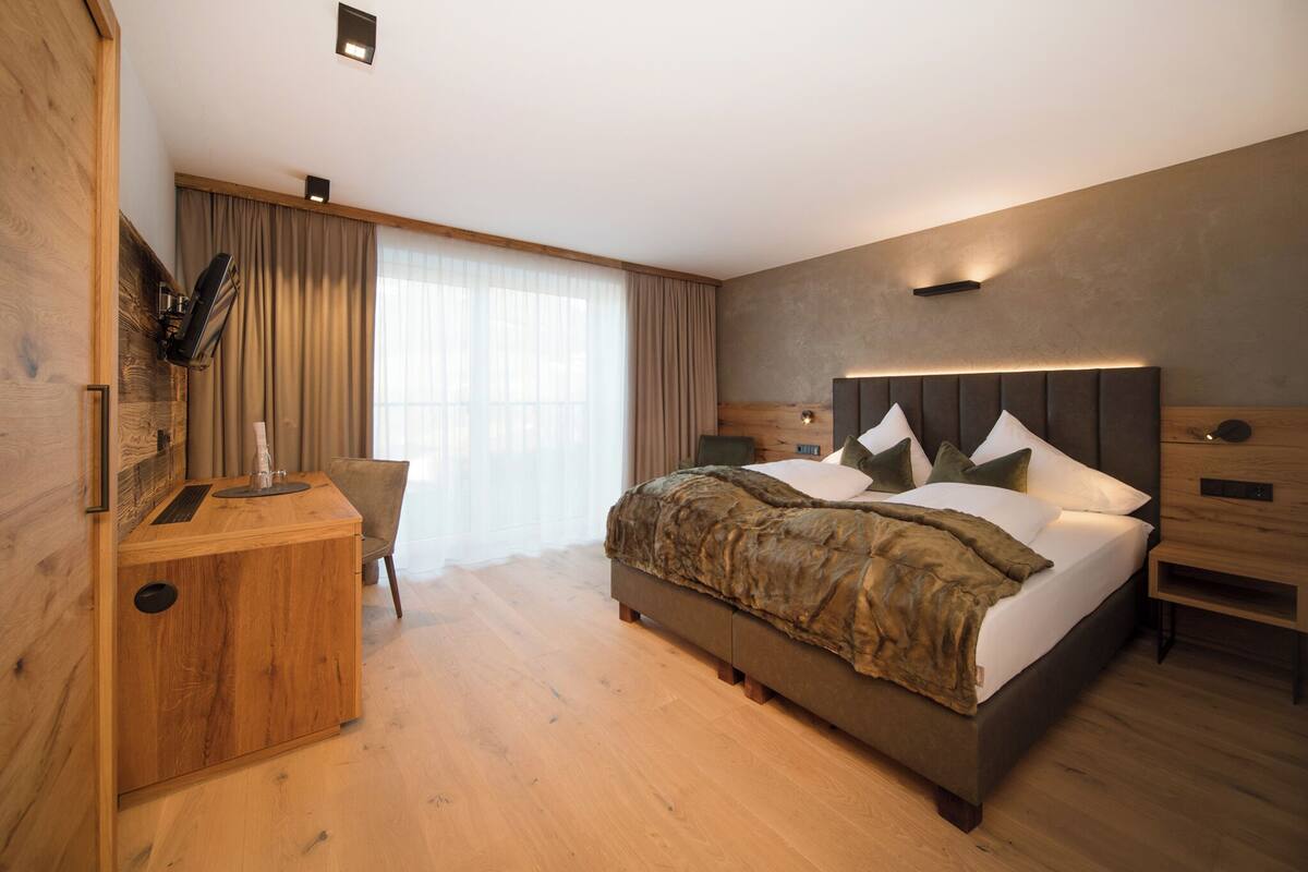 A modern hotel room with a large bed, wooden furniture, and a view of the outdoors.