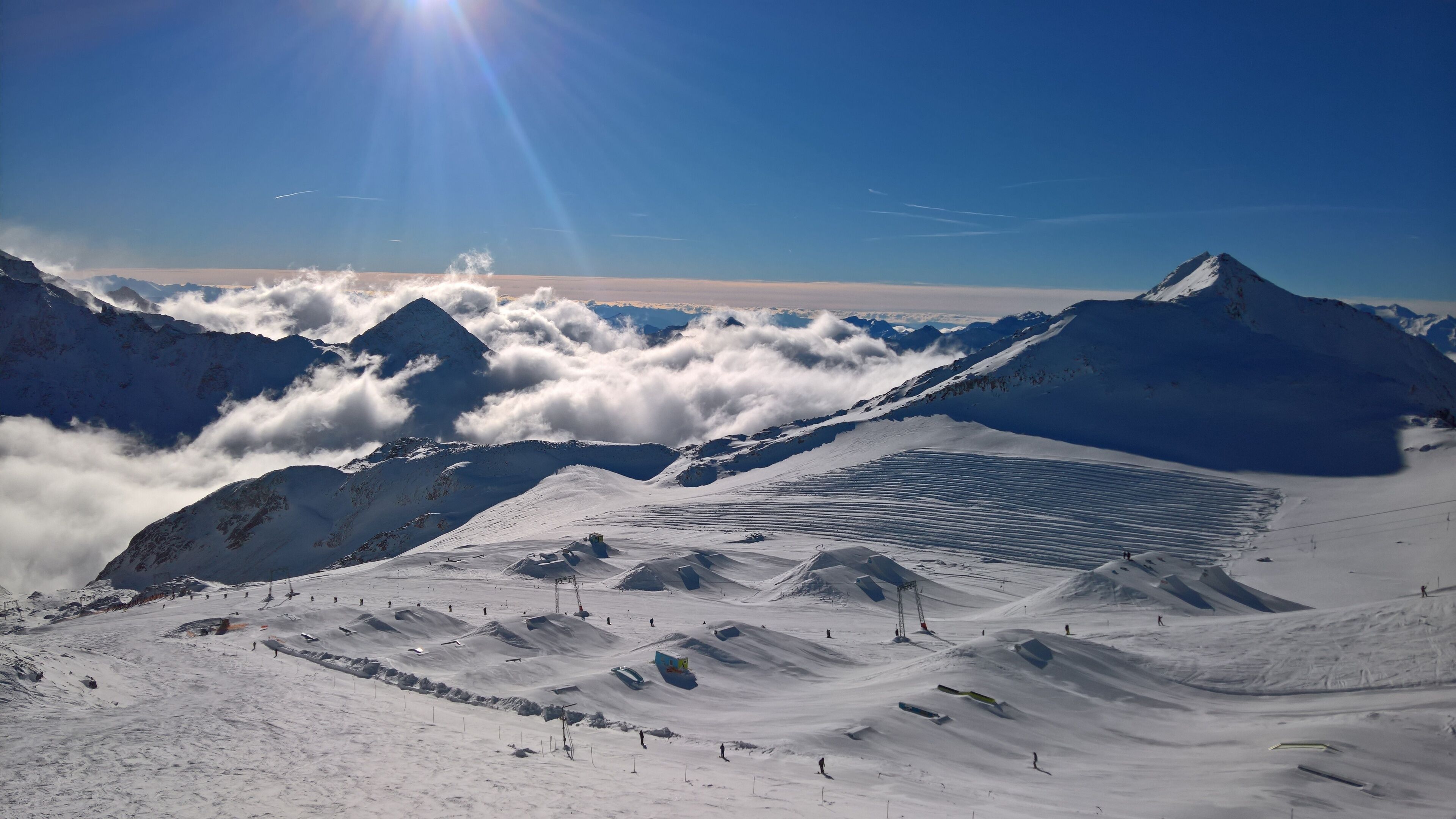 Eine verschneite Berglandschaft mit einer Skipiste, blauem Himmel und fernen Berggipfeln.