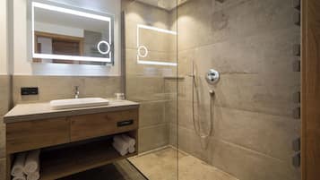 A modern bathroom with a glass-enclosed shower, a wooden vanity with a mirror, and a built-in shelf for towels.